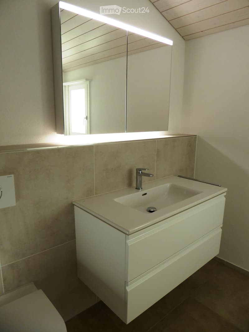 Modern bathroom with a white sink, chrome faucet, large mirror with built-in lighting, and a white cabinet below the sink.
