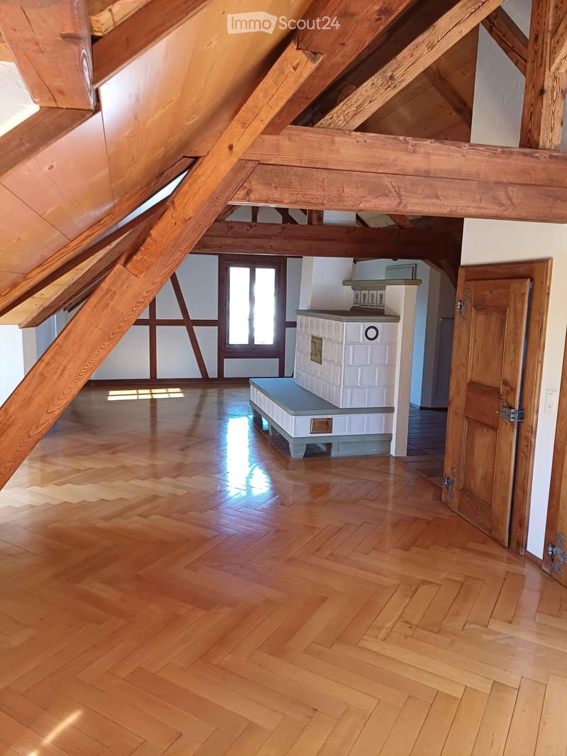 Empty room with wooden floor, exposed wooden beams, and a small white cabinet with a mirror on top.