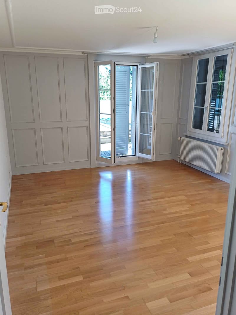 Empty room with wooden flooring, large windows, and double doors leading outside. No furniture or equipment present.