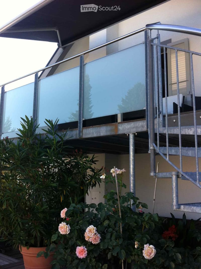 Balcony with glass railing, metal handrail, and potted plants with flowers below.
