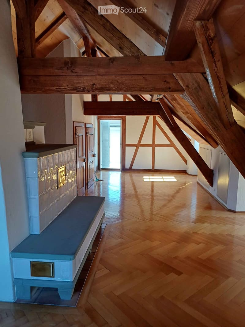 Bright, airy hallway with wooden floors, exposed wooden beams, and a blue bench along one wall. Natural light streams in from a doorway at the end.