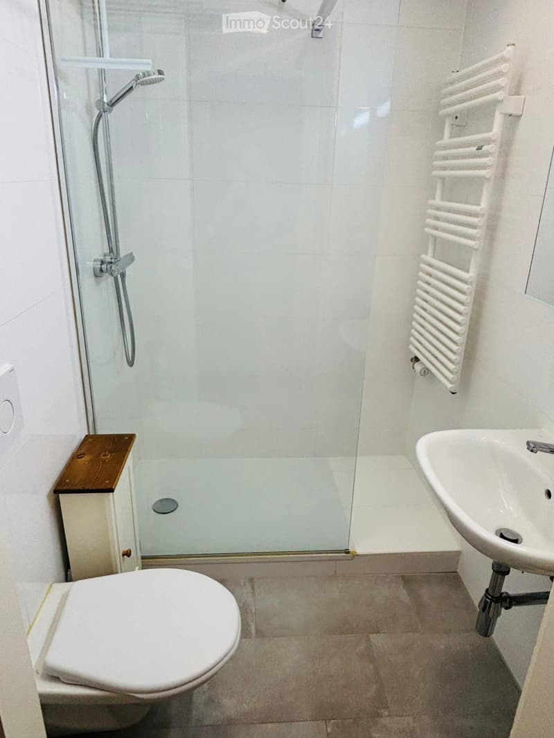 tiled floor, white shower, white sink, silver faucet, white toilet, white wall, wooden cabinet