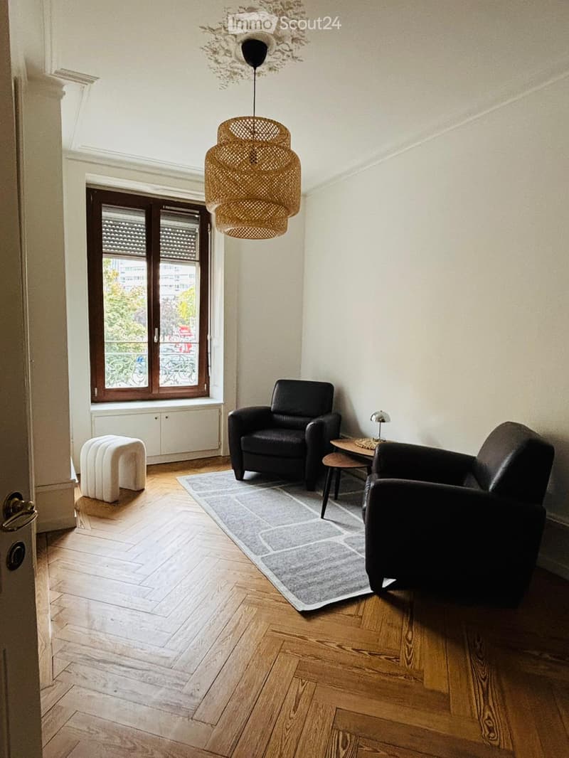 A room with two armchairs, a coffee table, a carpet, a floor lamp, and a window with view to outside.