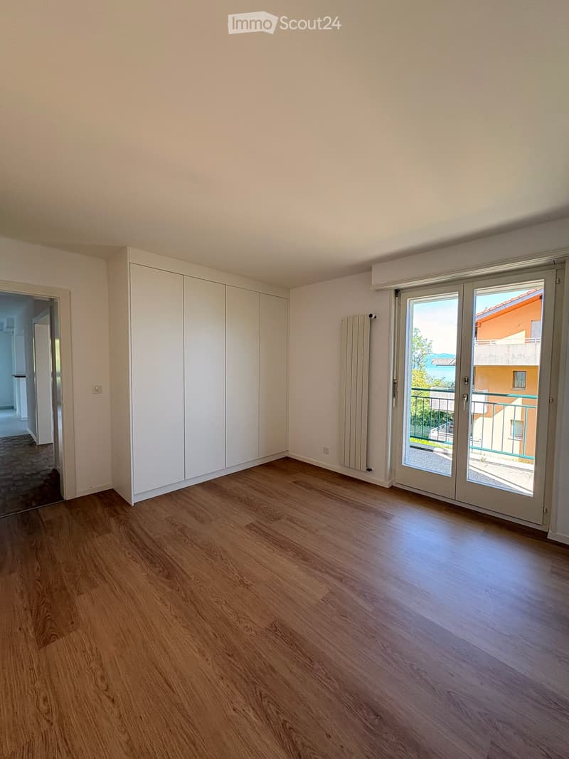 Empty room with wooden flooring, white walls, built-in closet, radiator, and large sliding glass door leading to a balcony.