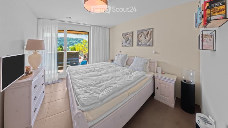 Bright bedroom with a large bed, nightstands, a dresser, a lamp, and a view through large windows.