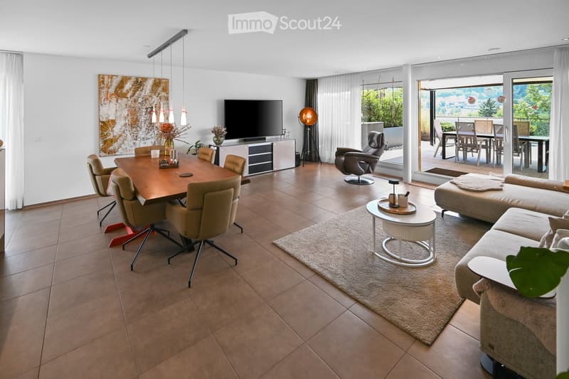 Modern living and dining area with a large sofa, coffee table, dining table with chairs, television, floor lamp, and artwork on the wall. The space features large windows with a view and a balcony area visible in the background.