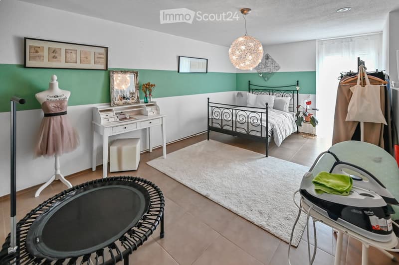 Cozy bedroom with a metal-framed bed, white desk, mannequin, framed pictures, and a hanging light fixture.