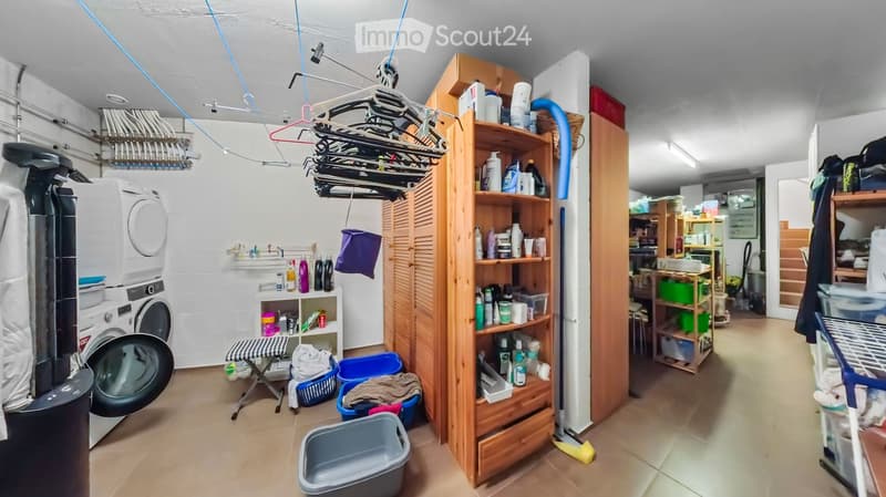 Laundry room with washing machine, drying rack, shelves filled with cleaning supplies, ironing board, and various storage items.