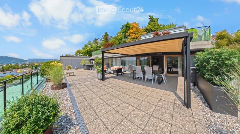 A modern outdoor terrace with a dining area, seating, and potted plants, overlooking a scenic landscape.