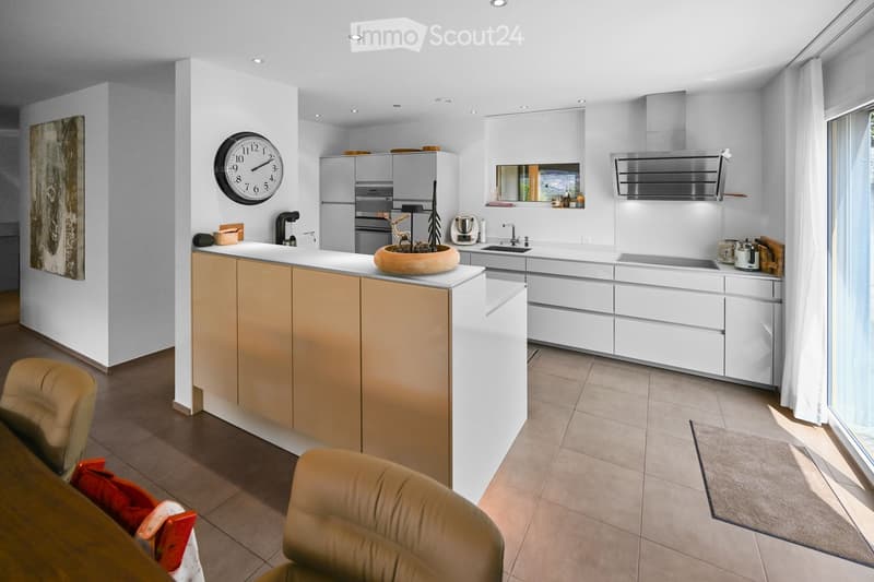 Modern kitchen with white and light wood cabinets, stainless steel appliances, a central island, and a seating area with a table and chairs.