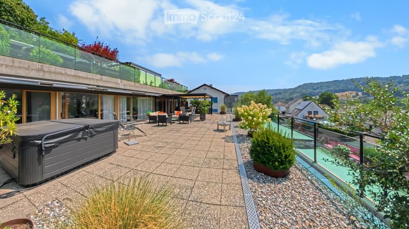 A spacious outdoor area with a hot tub, seating area, and a view of the surrounding landscape.