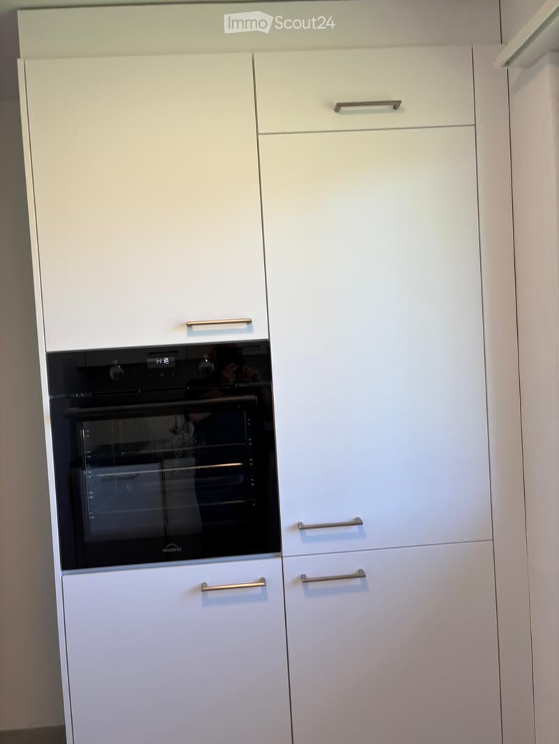 Modern kitchen with white cabinets and a built-in oven. The oven has a digital display and stainless steel handles.