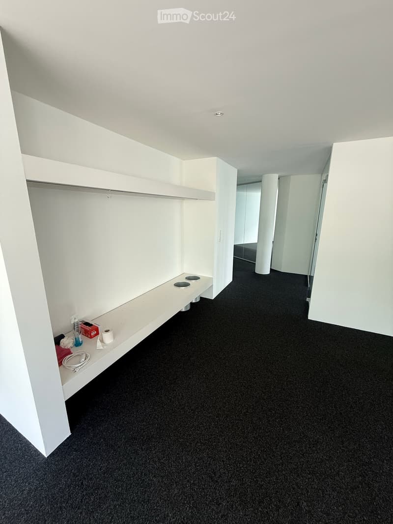 Empty room with white walls, black carpeted floor, built-in white shelving unit, and a small bench with built-in storage compartments.