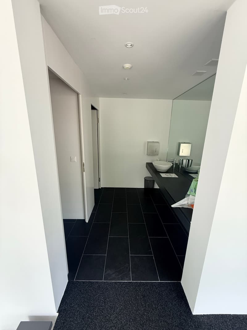 Modern bathroom with black tiled floor, white walls, and a black countertop sink area with a mirror and storage.