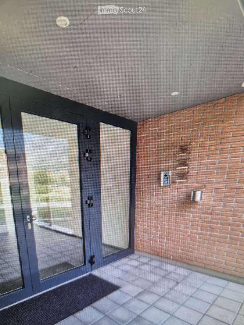 Empty hallway with tiled floor, brick wall, and glass double doors leading outside.
