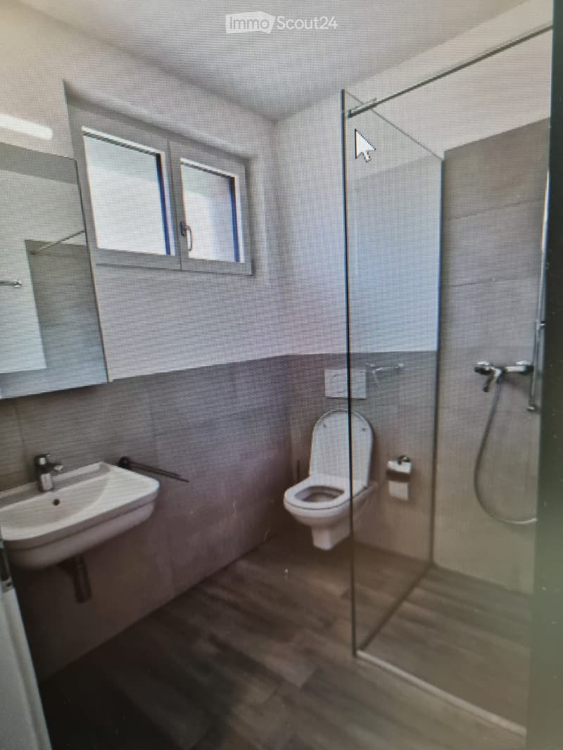 Modern bathroom with a glass-enclosed shower, a white toilet, and a white sink with a modern faucet. The walls are tiled in a two-tone design, and the floor is dark.