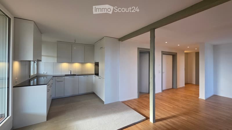 Modern kitchen with white cabinets, a central island, and wooden flooring. The space is well-lit with recessed lighting and features a sleek, minimalist design.