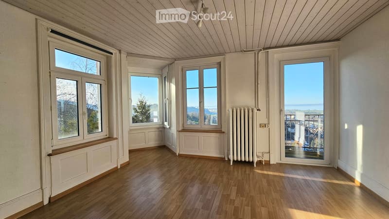 Empty room with wooden flooring, white walls, multiple windows, radiator, and a door leading to a balcony.