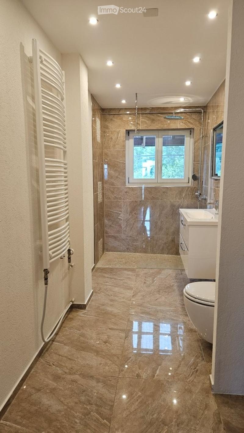 Modern bathroom with marble tiles, a large window, a toilet, a sink, a shower, and a radiator.