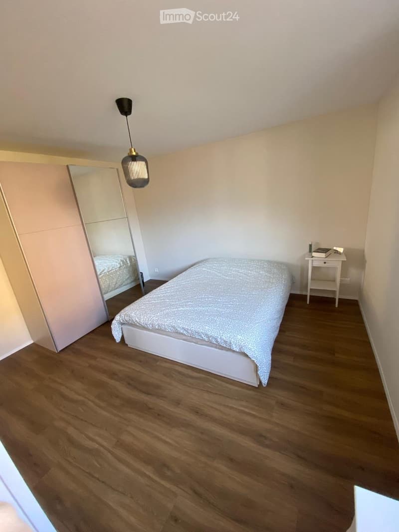 Minimalist bedroom with a single bed, white wardrobe, small nightstand, and a hanging lamp.