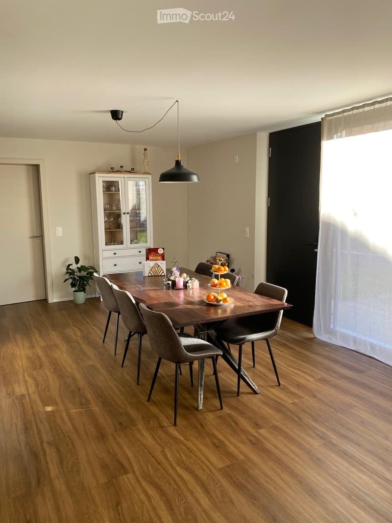 Dining room with wooden floor, modern dining table, six chairs, pendant light, white cabinet, and a small plant in a pot.