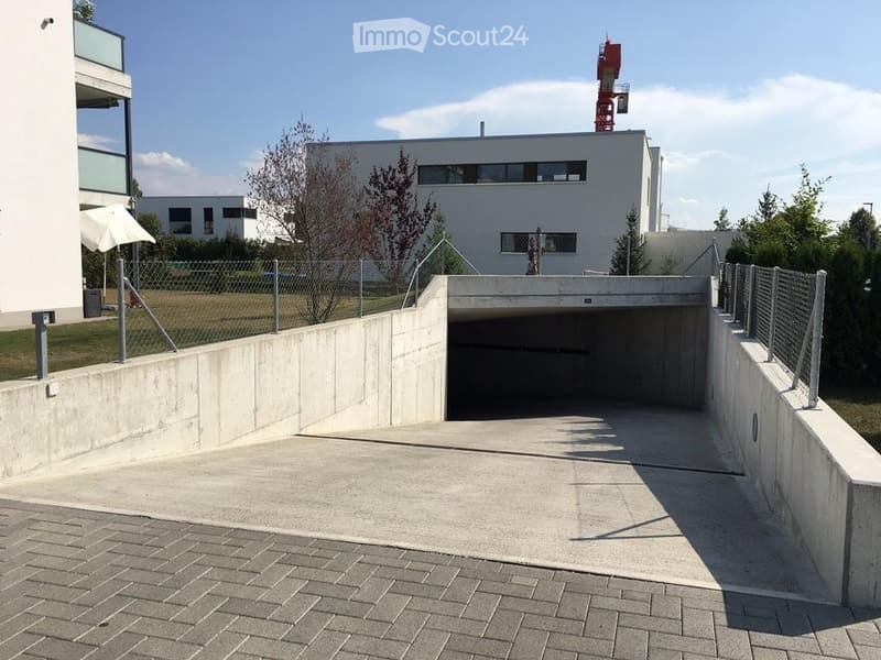 Modern building entrance with a covered garage area, concrete walls, and a fenced perimeter.