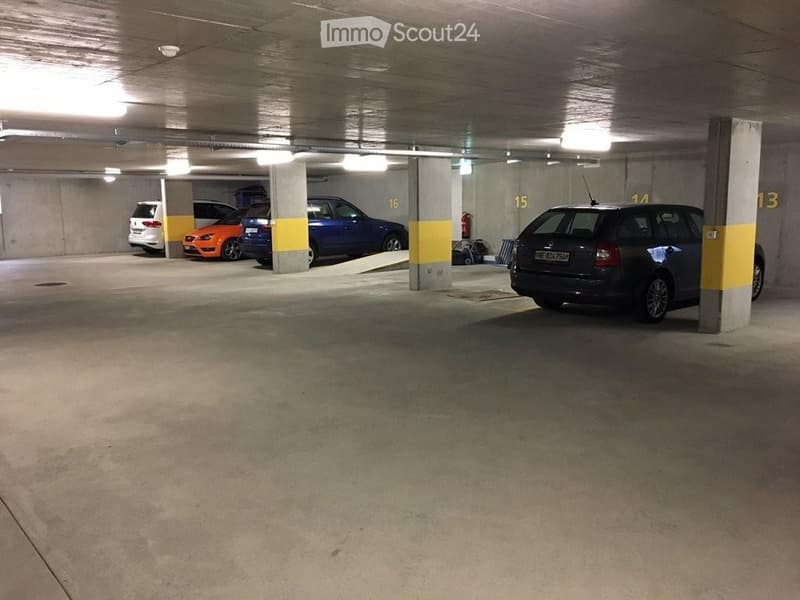 Underground parking area with several parked cars, concrete pillars, and numbered parking spots.
