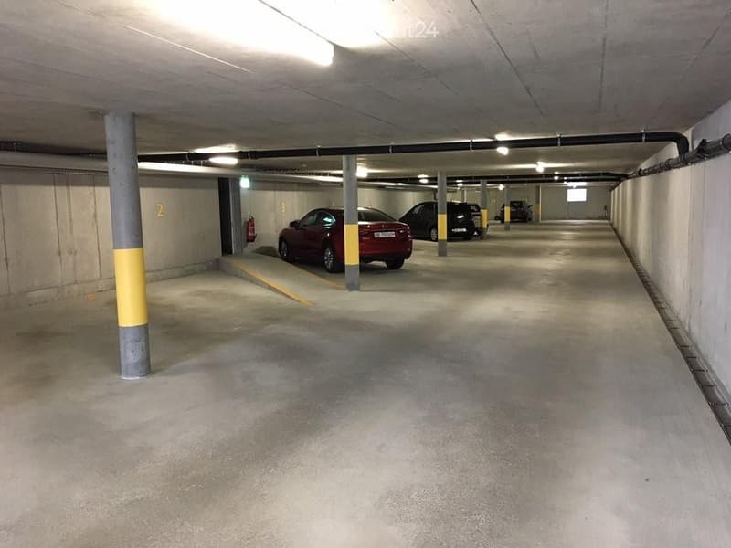 Underground parking area with several parked cars, concrete pillars, and fluorescent lighting.