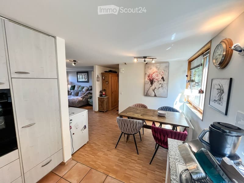 A modern, open-plan living and dining area with light wood flooring, white cabinets, a dining table with chairs, a sofa, and a coffee maker on the counter.