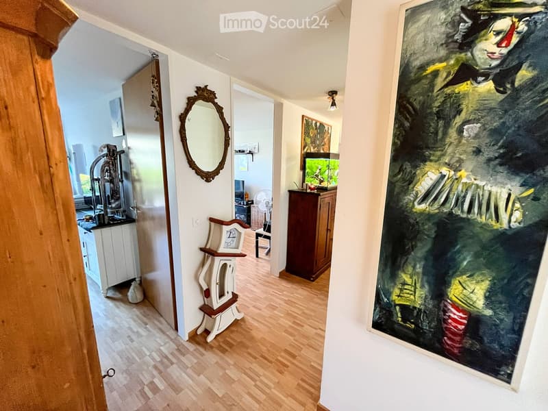 Hallway with wooden flooring, white walls, a large painting, a small table with a clock, a mirror, and a fish tank in the adjacent room.