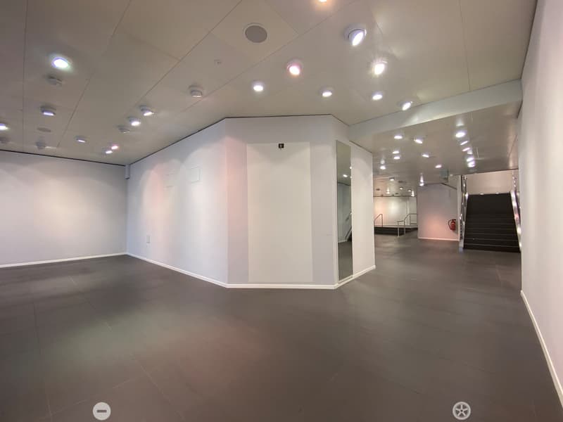 Empty room with white walls, dark tiled floor, and recessed lighting. A staircase leads to another level.