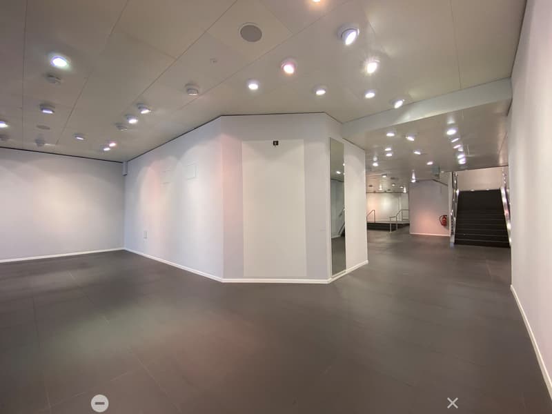 Empty room with white walls, dark tiled floor, and recessed lighting. A staircase leads to another level.