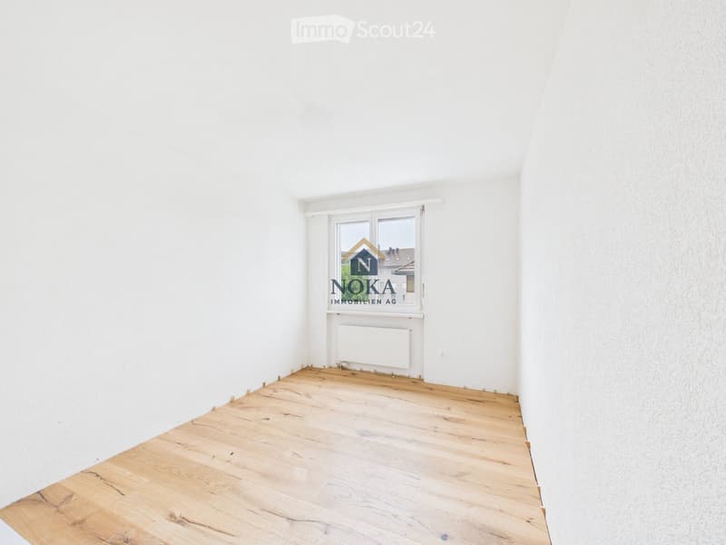 Empty room with white walls, wooden floor, and a window with a radiator below it.
