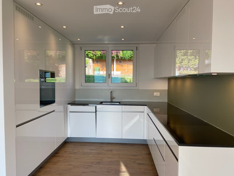 Modern kitchen with white cabinets, black countertops, and a wooden floor. Features a sink, faucet, and built-in oven.