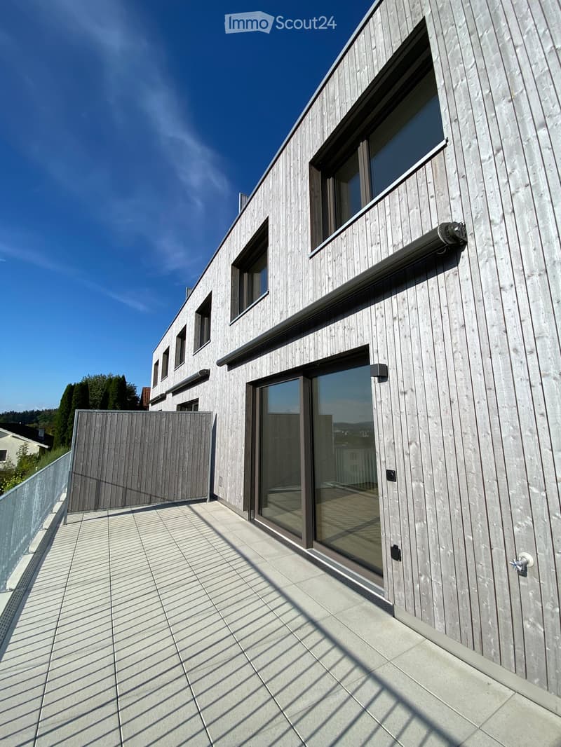 Modern wooden house with large windows and a tiled balcony area.