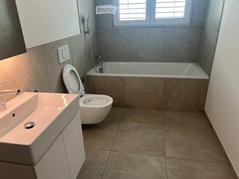 Modern bathroom with a white sink, chrome faucet, toilet, and bathtub, featuring tiled walls and floor.