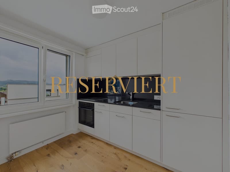 Modern kitchen with white cabinets, wooden flooring, large windows, and stainless steel appliances including a sink, oven, and faucet.