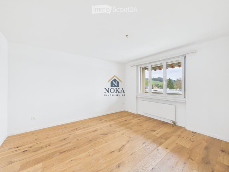 Empty room with light wooden flooring, white walls, and large windows offering a scenic view.