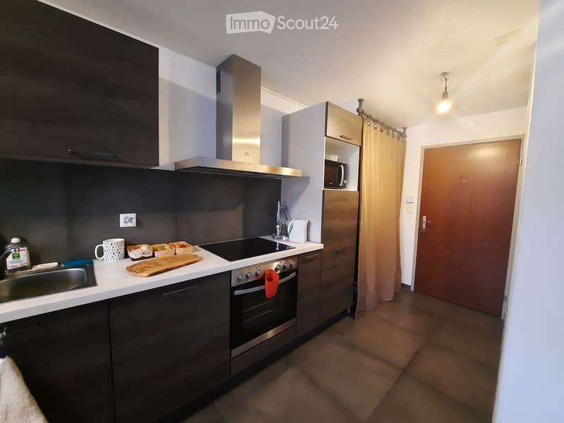 Modern kitchen with stainless steel appliances, black cabinets, and white countertops. Includes a sink, oven, microwave, refrigerator, and various kitchen items on the counter.