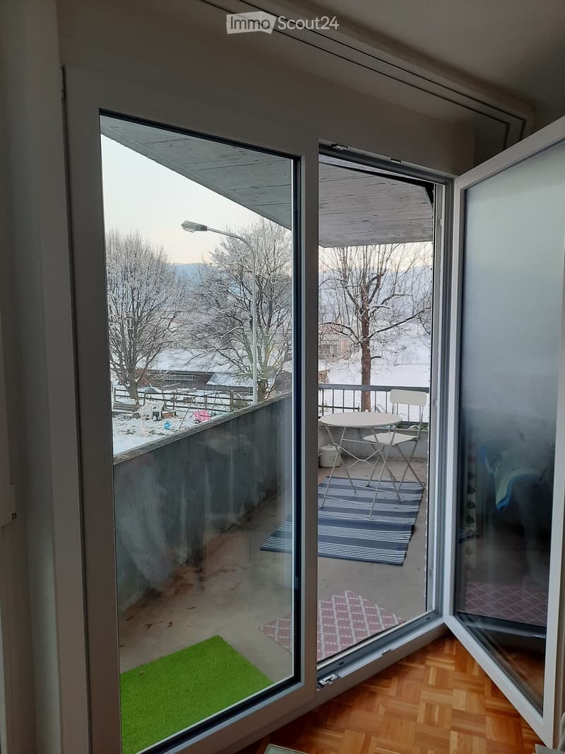 Balcony with a small table and two chairs, overlooking a snowy landscape with trees and a streetlight.