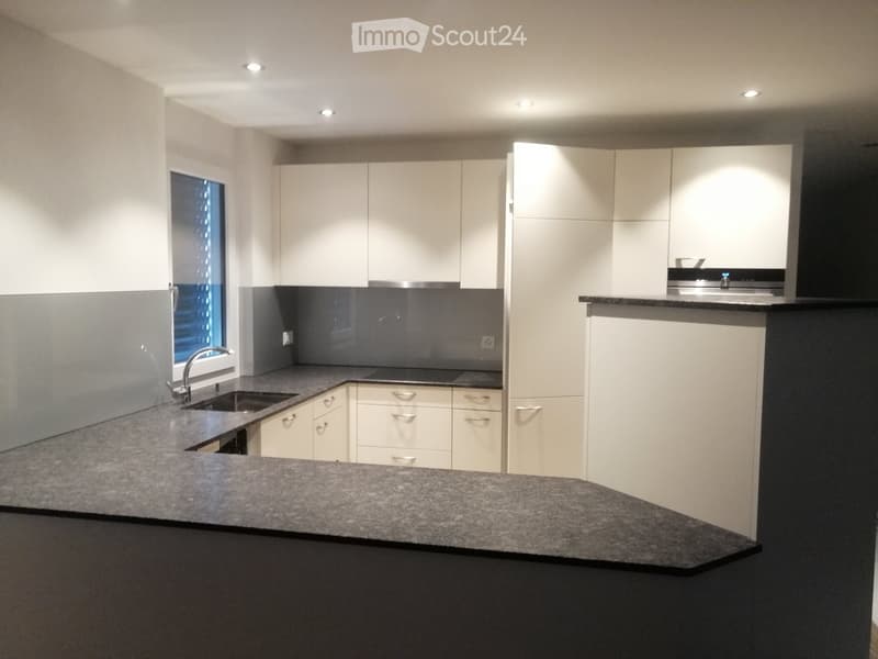 Modern kitchen with white cabinets, dark countertops, and a central island. Features a sink with a modern faucet and built-in storage drawers.