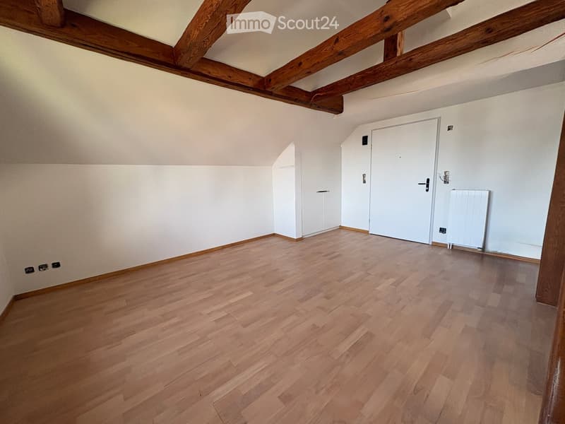 Empty attic room with wooden floors, white walls, exposed wooden beams, and two white doors.