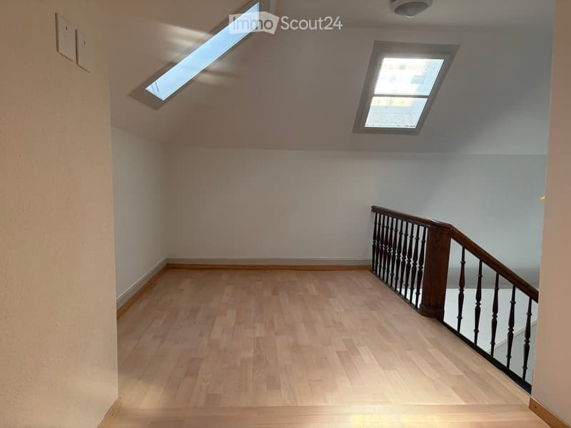 Empty hallway with wooden flooring, light-colored walls, and two skylight windows at the top. A wooden staircase with a dark railing is visible on the right side.