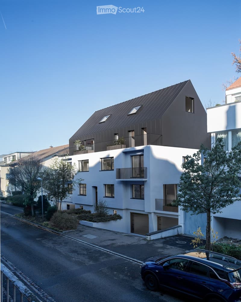 modern building, multiple stories, large windows, balconies, black roof, garage