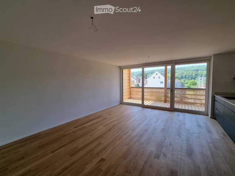 Empty room with wooden flooring, large sliding glass doors leading to a balcony, and a view of the surrounding area.