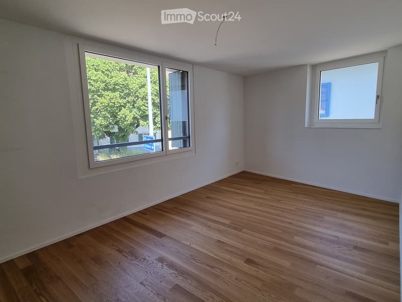 Empty room with wooden flooring and white walls, featuring two windows with white frames and blinds.