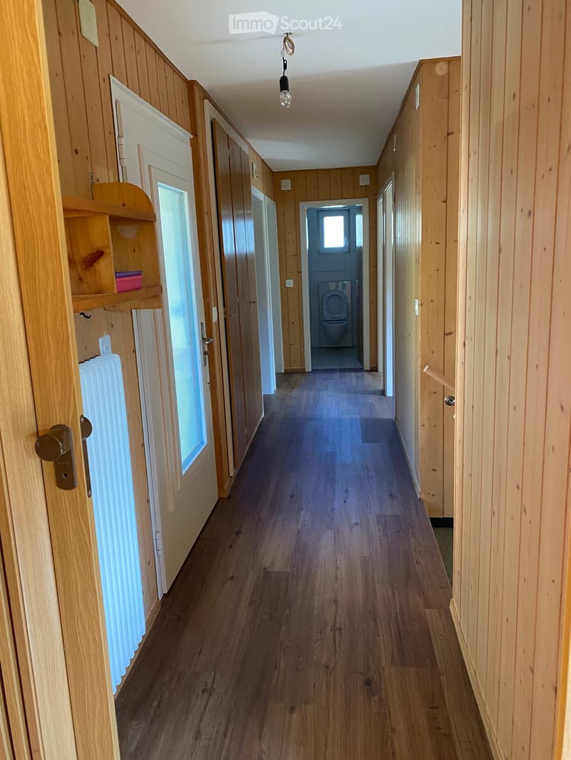 Wooden hallway with wooden walls, wooden floor, and several doors leading to rooms, including a visible bathroom.