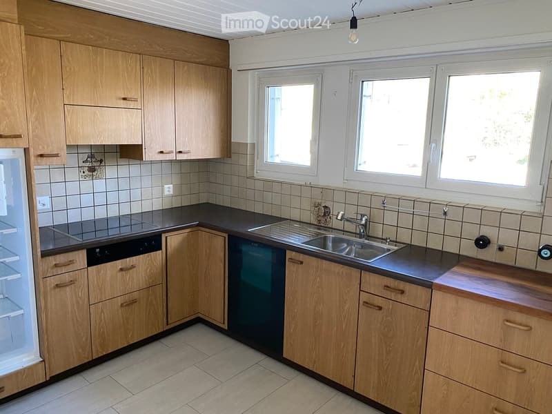 Modern kitchen with light wooden cabinets, stainless steel sink, dishwasher, and refrigerator. Tiled backsplash and countertops.