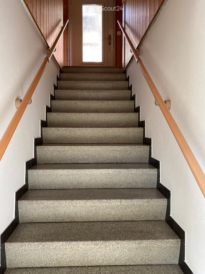 Staircase with grey concrete steps and wooden handrails, leading to a doorway with a window above it.