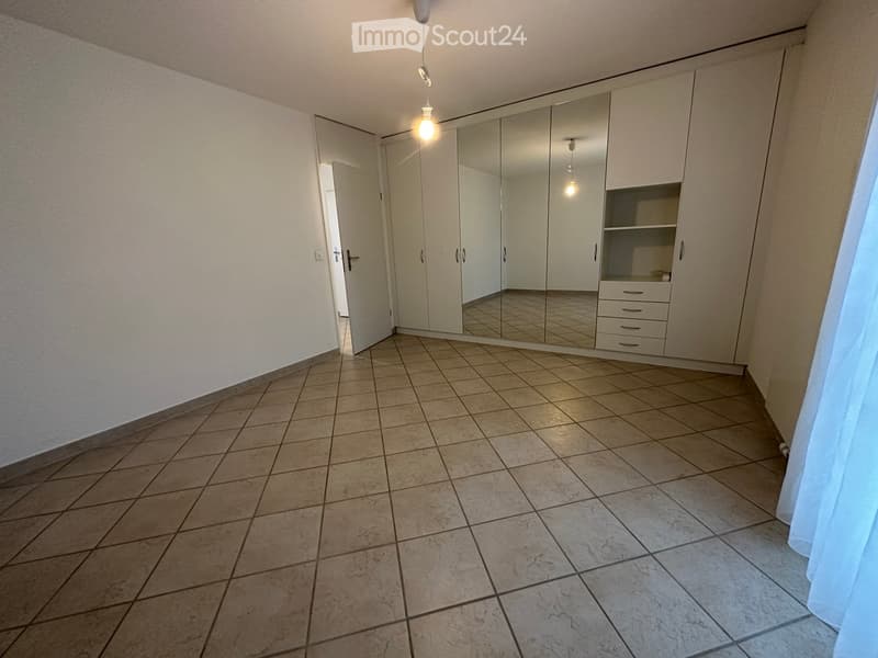 Empty room with tiled floor, white walls, built-in wardrobe with mirrored doors, and a small shelf unit.
